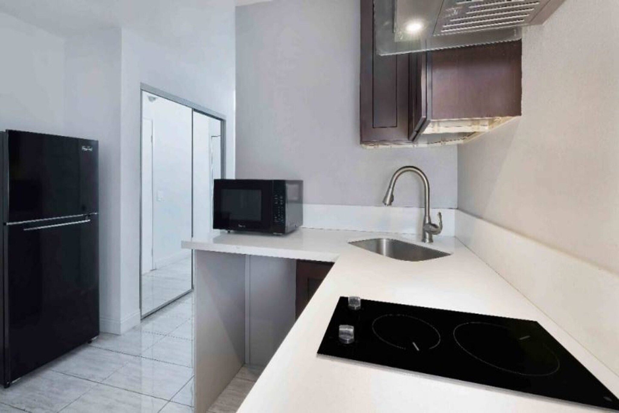 A modern kitchen with a black refrigerator, a microwave, a sink, and a built-in stovetop.