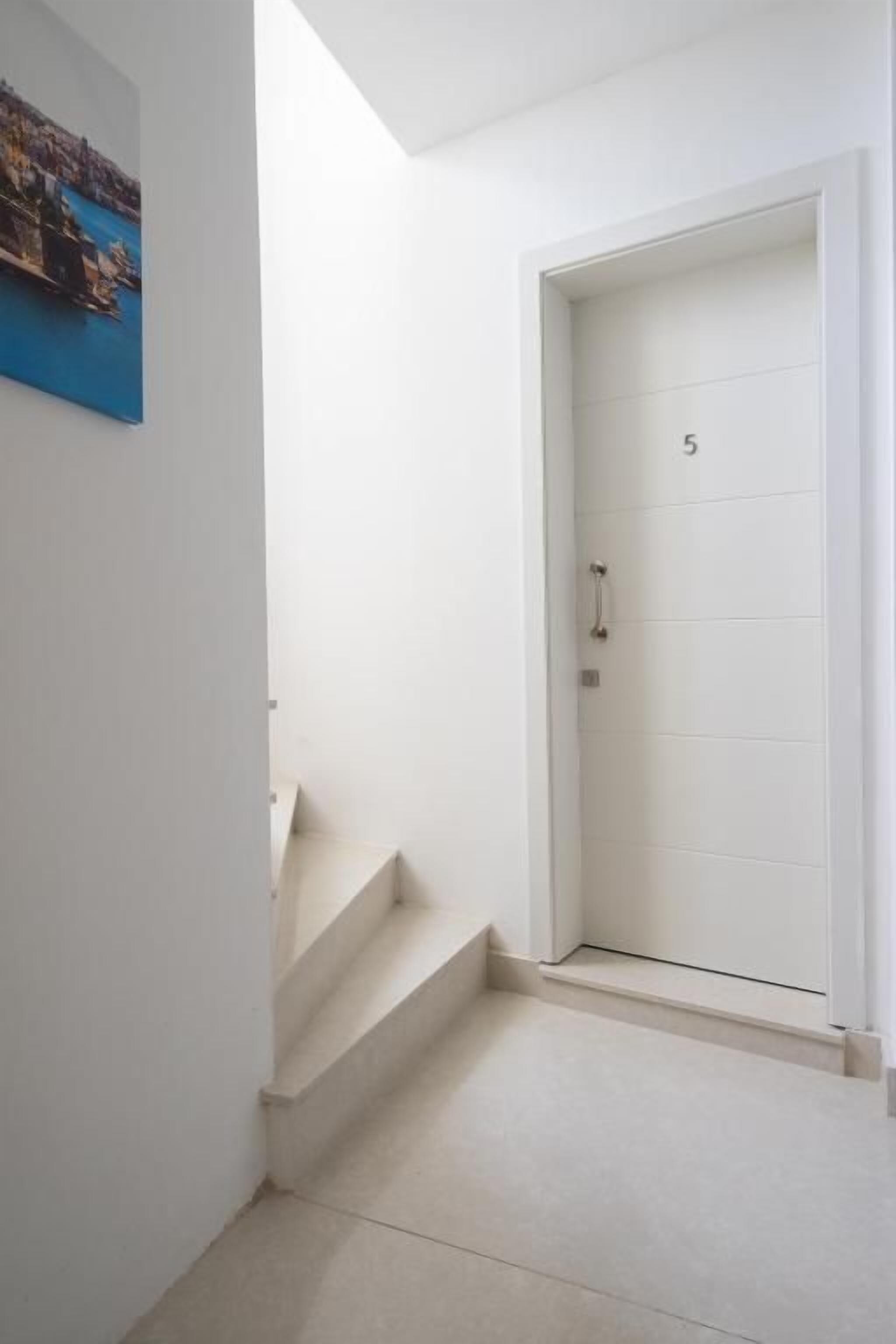 Eine weiße Tür mit der Nummer 5, eine Treppe, die zu einer oberen Etage führt, und ein Gemälde an der Wand.