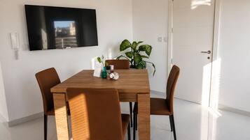 A modern dining area with a wooden table and brown chairs, a flat-screen TV mounted on the wall, and a potted plant on the table.