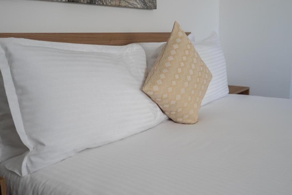 A bed with white bedding and a single patterned pillow.