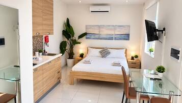 A modern hotel room with a bed, bedside tables, a desk, and a glass dining table.