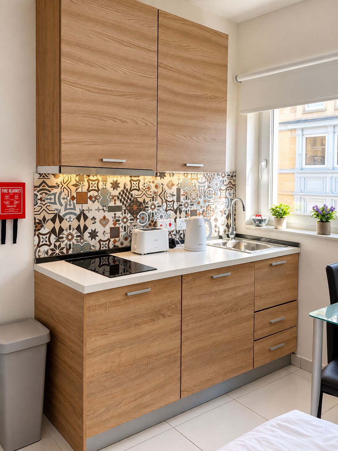 A modern kitchen with wooden cabinets, a patterned backsplash, and a window with a view of buildings.