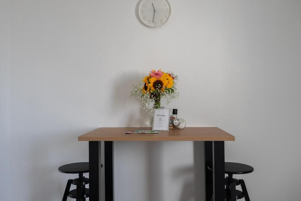 A small table with a clock, a welcome sign, and a vase with flowers.