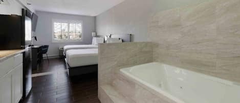 A modern bathroom with a large bathtub, a shower area, and a separate bedroom with a bed and a desk.