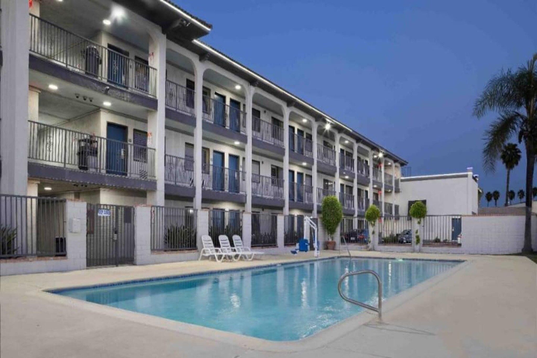 Un hôtel à plusieurs étages doté d’une piscine, d’un espace extérieur aménagé et d’une façade blanche.
