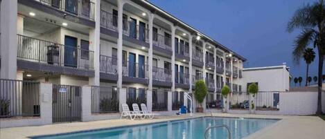 A multi-story hotel with a swimming pool, outdoor seating, and a white exterior.