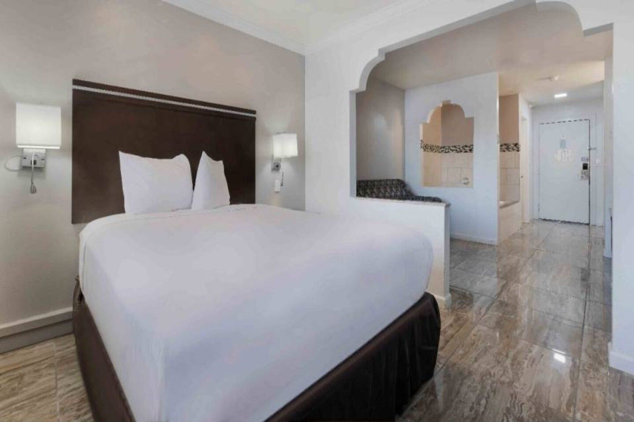 Une chambre d’hôtel avec un grand lit, une tête de lit, deux lampes fixées au mur et un sol en marbre.