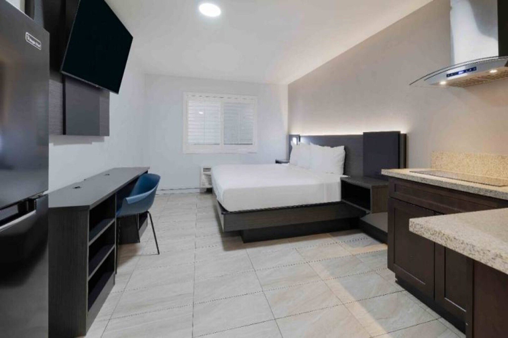 Una habitación de hotel moderna con cama, escritorio, silla, televisor y kitchenette.