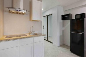 Eine moderne Küche mit weißen Schränken, einer Edelstahl-Dunstabzugshaube, einem schwarzen Kühlschrank und einer Glastür zu einem Essbereich.
