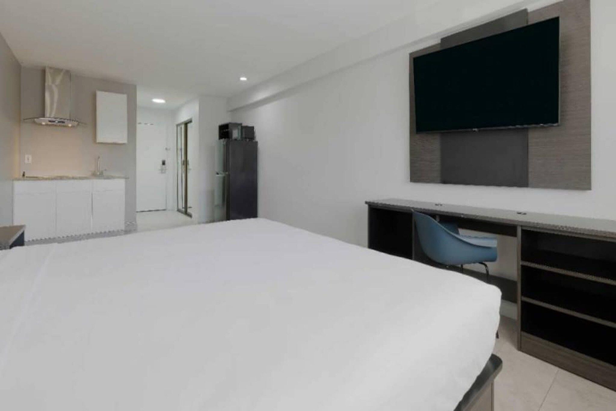 Ein Hotelzimmer mit einem Bett, einem Schreibtisch, einem Sessel, einem an der Wand befestigten Fernseher und einer Küchenzeile.