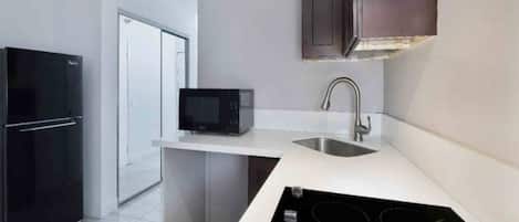 A compact kitchen with a black refrigerator, a microwave, and a sink with a modern faucet.