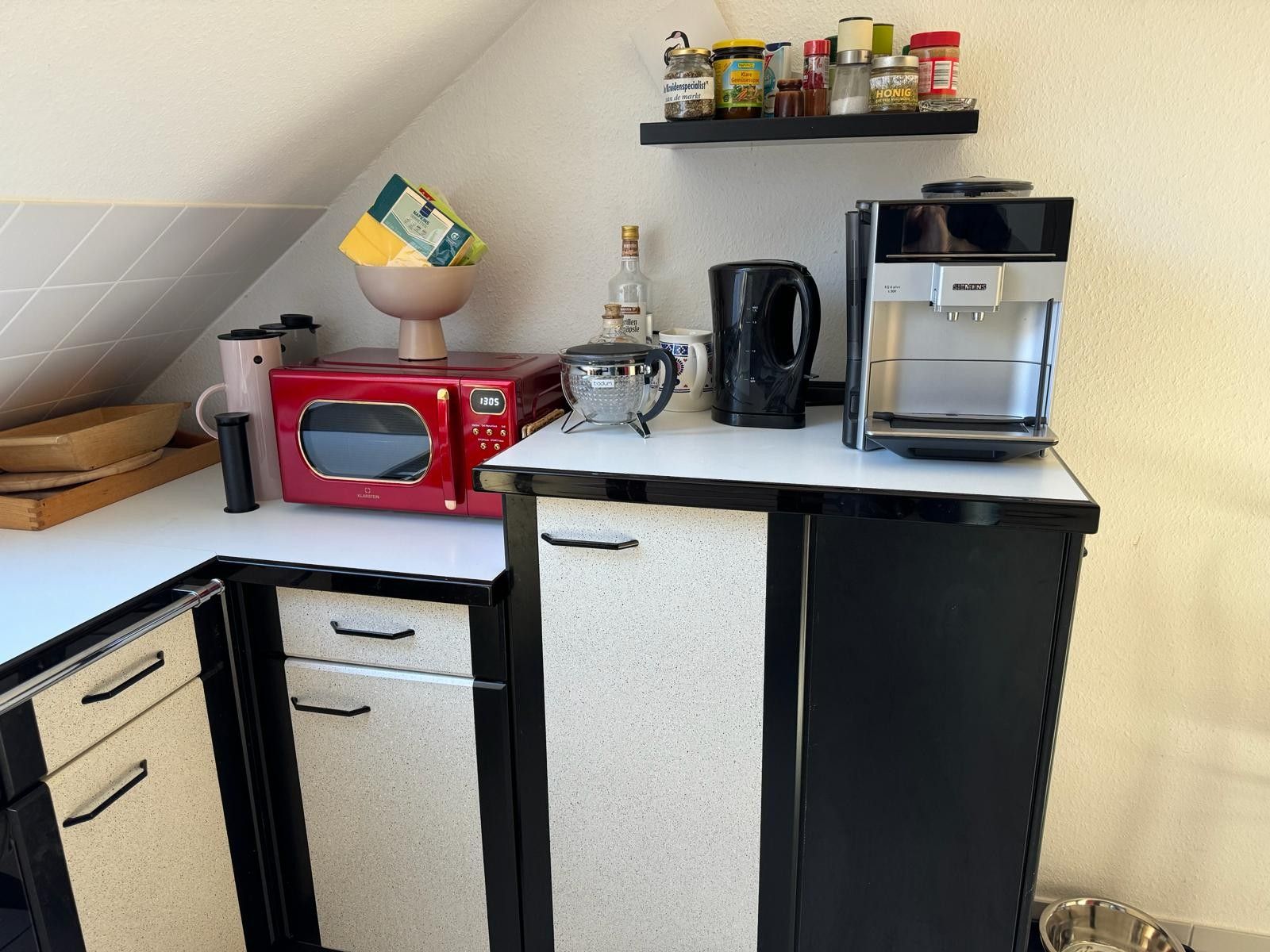 Une petite cuisine équipée d’un four à micro-ondes, d’une machine à café et d’une étagère avec des bocaux.