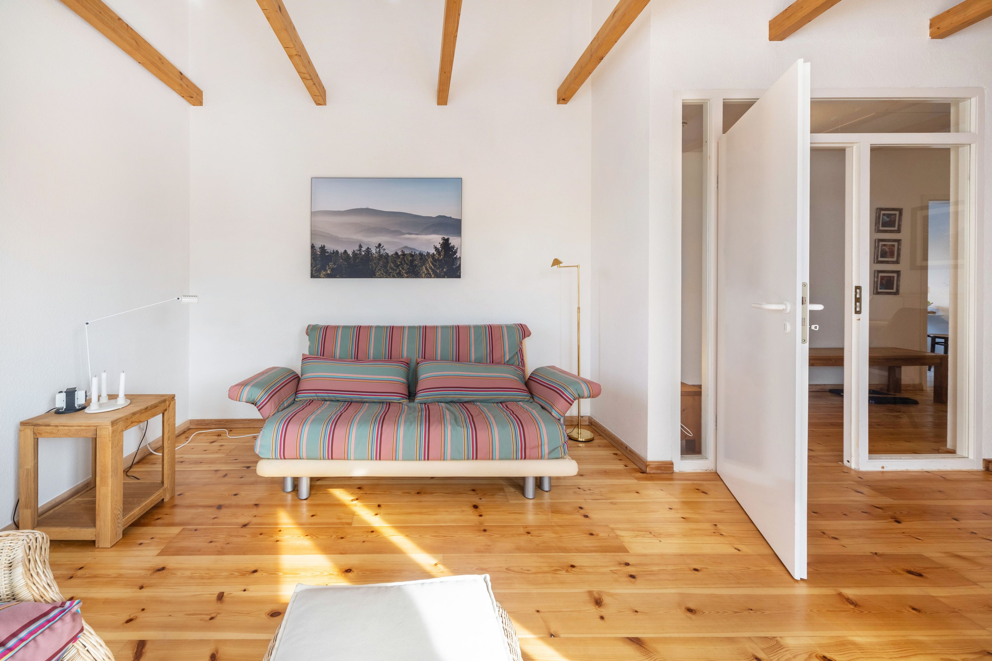 Ein Zimmer mit Holzboden, einer Couch mit gestreiften Kissen, einem Tisch mit Kerzen und einem Bild an der Wand.