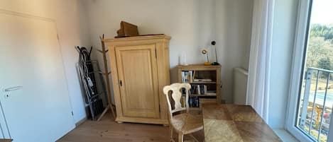 A room with a wooden floor, a wooden table with a woven chair, a cabinet, and a bookshelf.