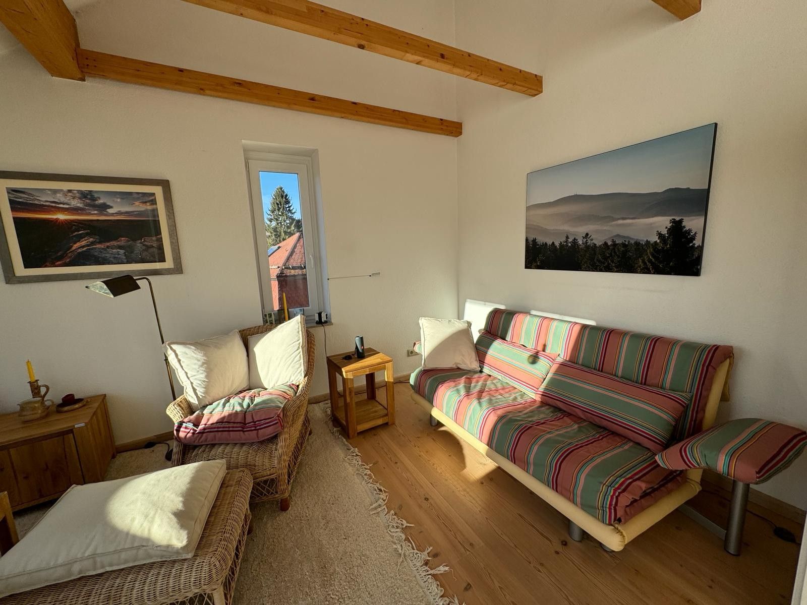Ein gemütliches Wohnzimmer mit einer Couch, zwei Sesseln, einem kleinen Tisch, einer Lampe und einem Fenster mit Blick auf ein Haus.