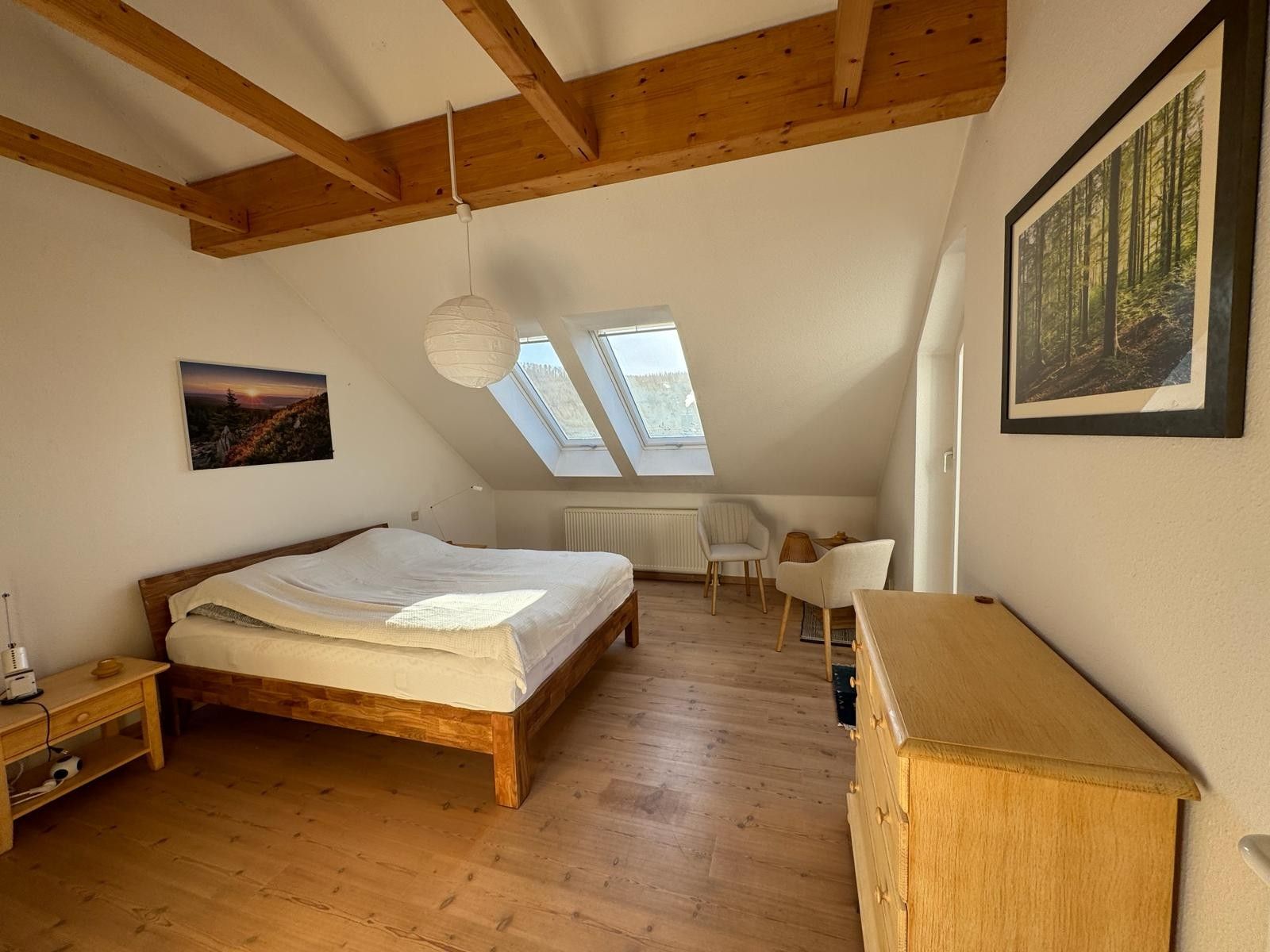 Ein Schlafzimmer mit einem hölzernen Bett, einem Schreibtisch, einem Stuhl und einem Oberlicht.