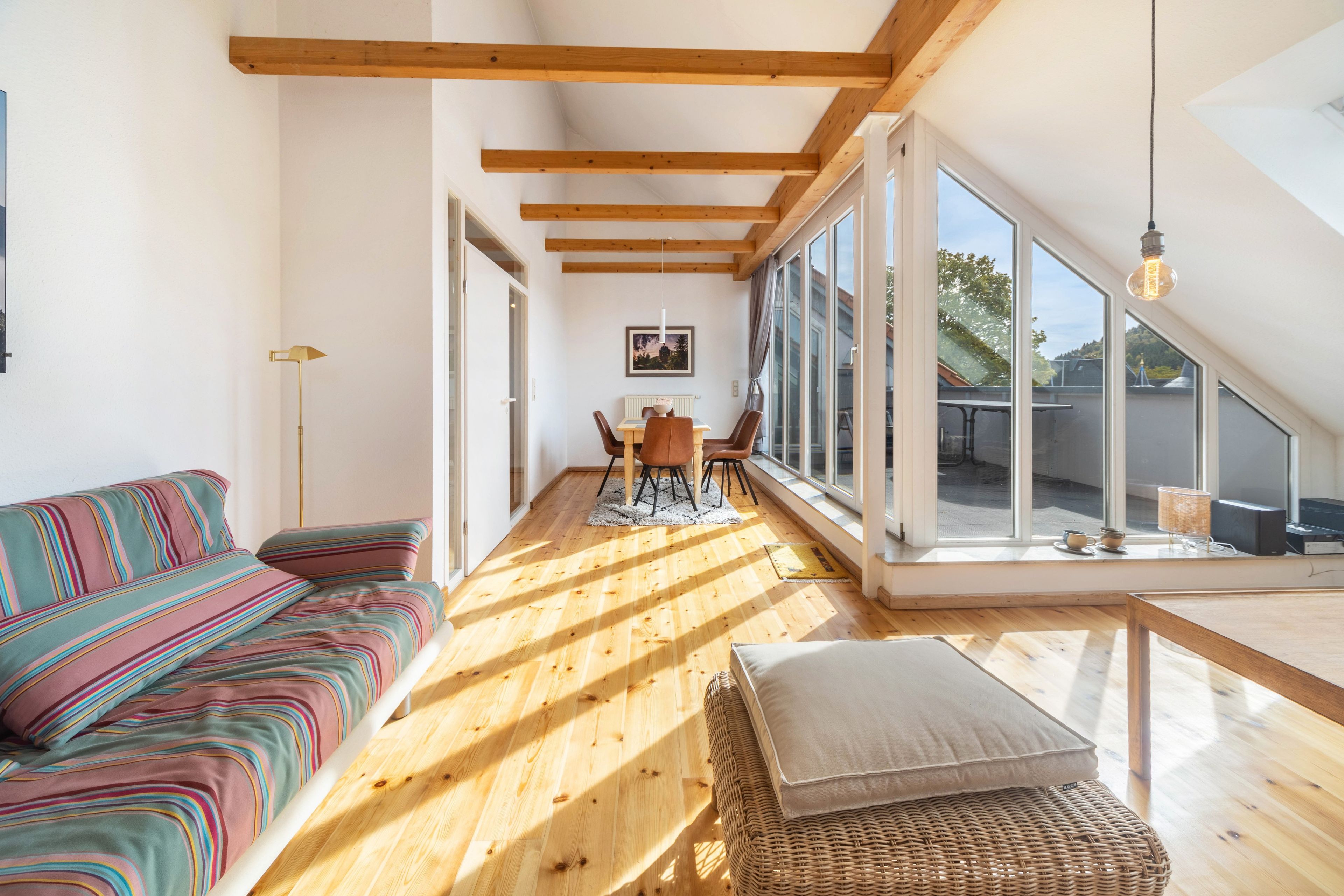 A modern interior with a wooden floor, a sofa, a dining table, and a large window.