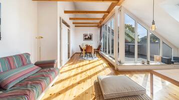 A modern interior with a wooden floor, a sofa, a dining table, and a large window.