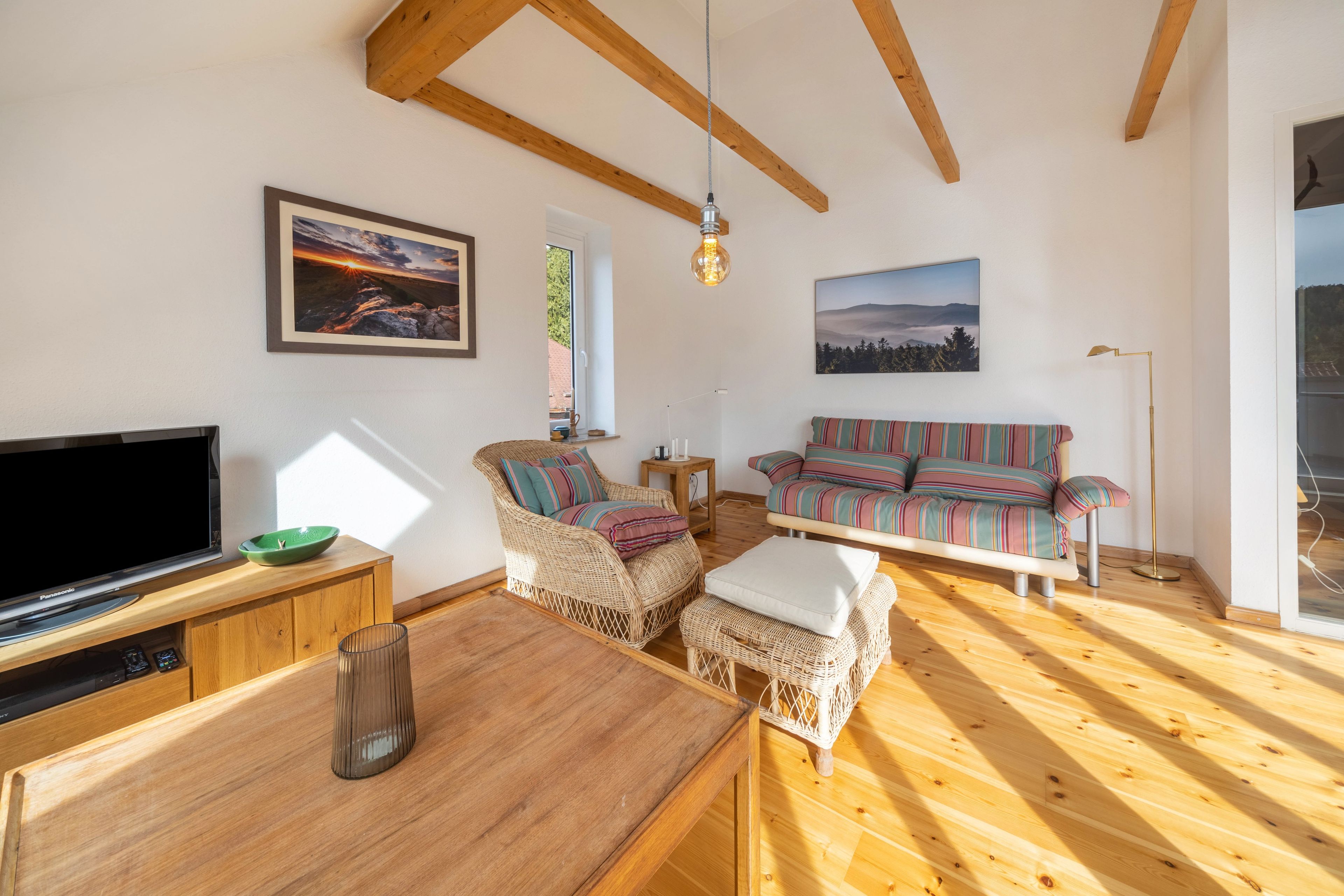 Een ruime woonkamer met houten vloer, een televisie, een bank en een eettafel.