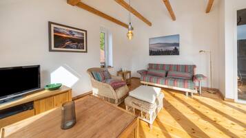 Een ruime woonkamer met houten vloer, een televisie, een bank en een eettafel.