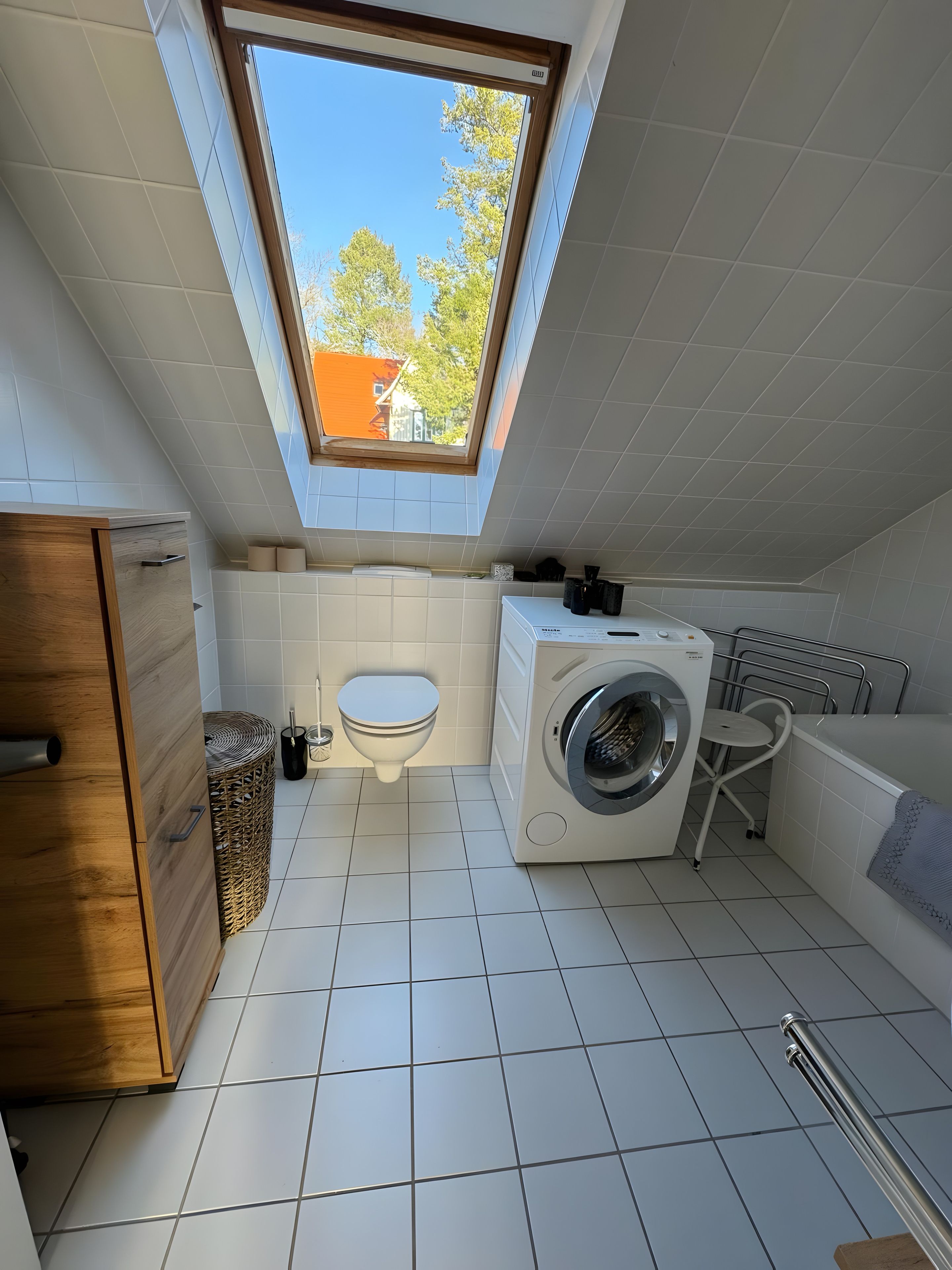 Ein kleines, modernes Badezimmer mit Dachfenster, einer Waschmaschine, einer Toilette und einer Badewanne.