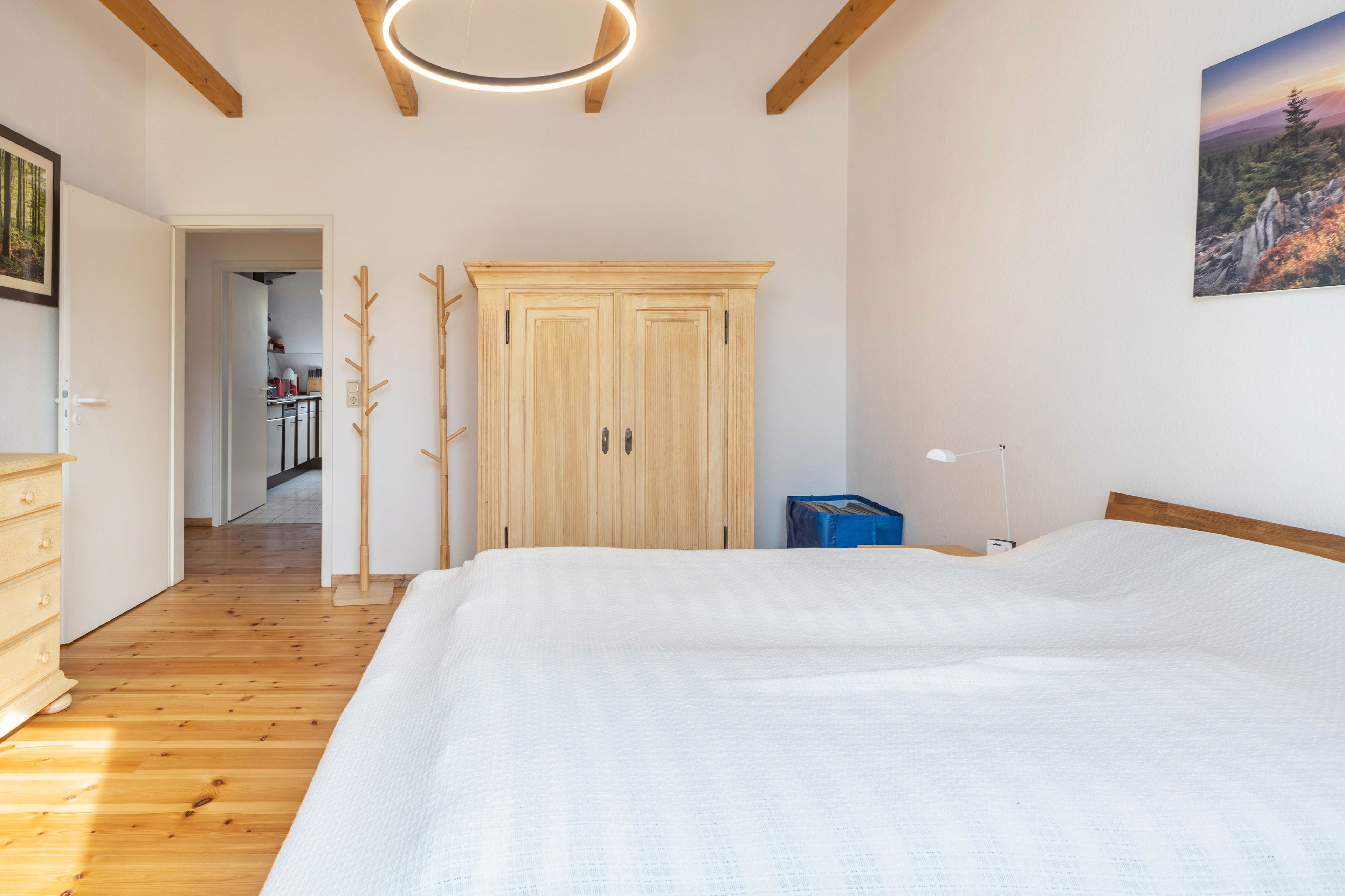 A bedroom with a large bed, wooden flooring, a wardrobe, and a painting on the wall.