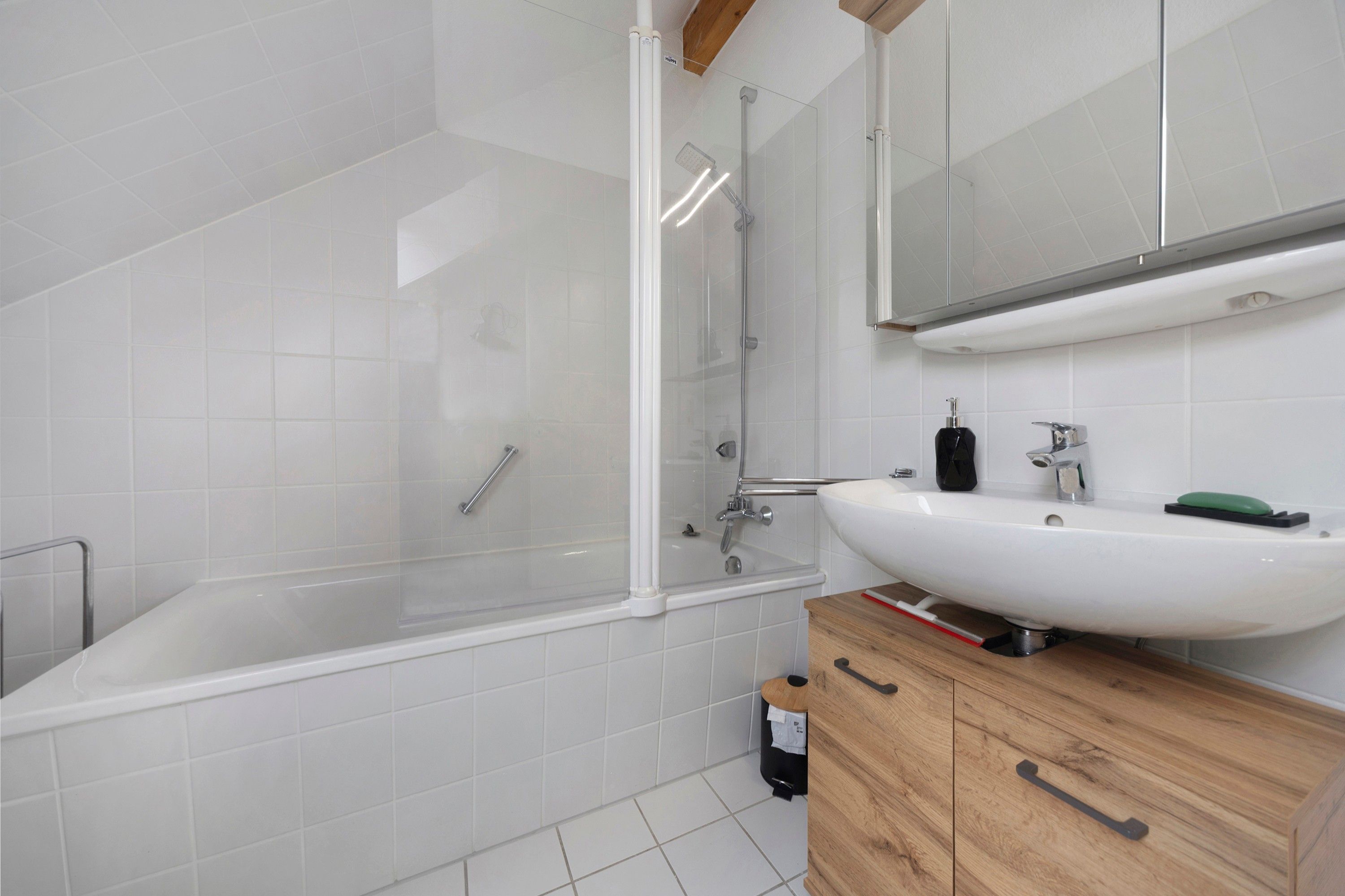 Ein modernes Badezimmer mit einer gläsernen Duschkabine, einem weißen Waschbecken und Holzschränken.