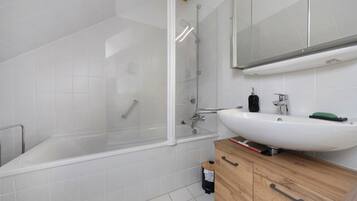 Ein modernes Badezimmer mit einer gläsernen Duschkabine, einem weißen Waschbecken und Holzschränken.