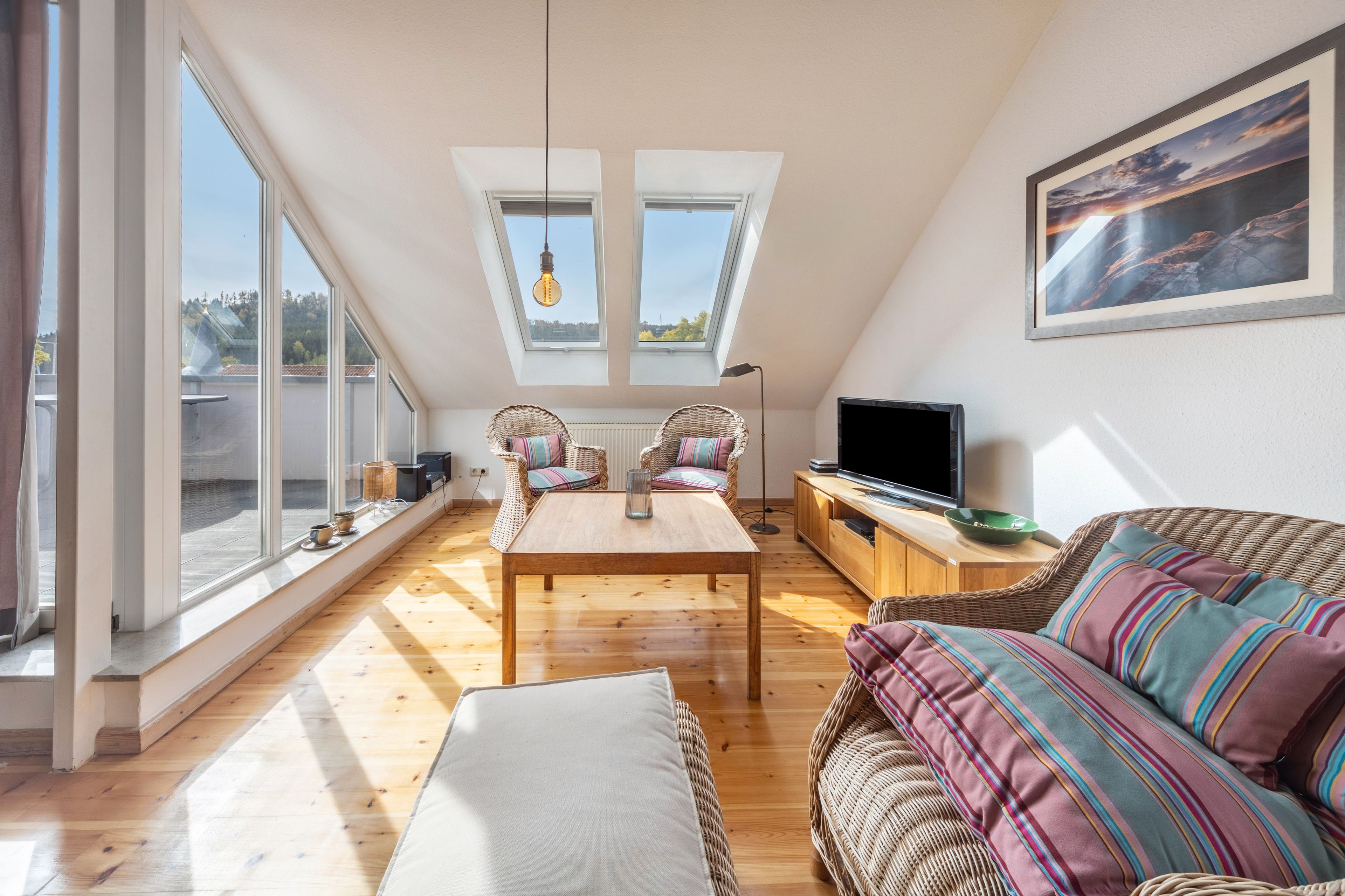 Ein geräumiges Wohnzimmer mit großen Fenstern, einem Fernseher und einem Gemälde an der Wand.