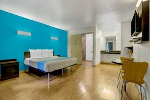 Quarto de hotel com cama, escrivaninha, cadeira e banheiro.