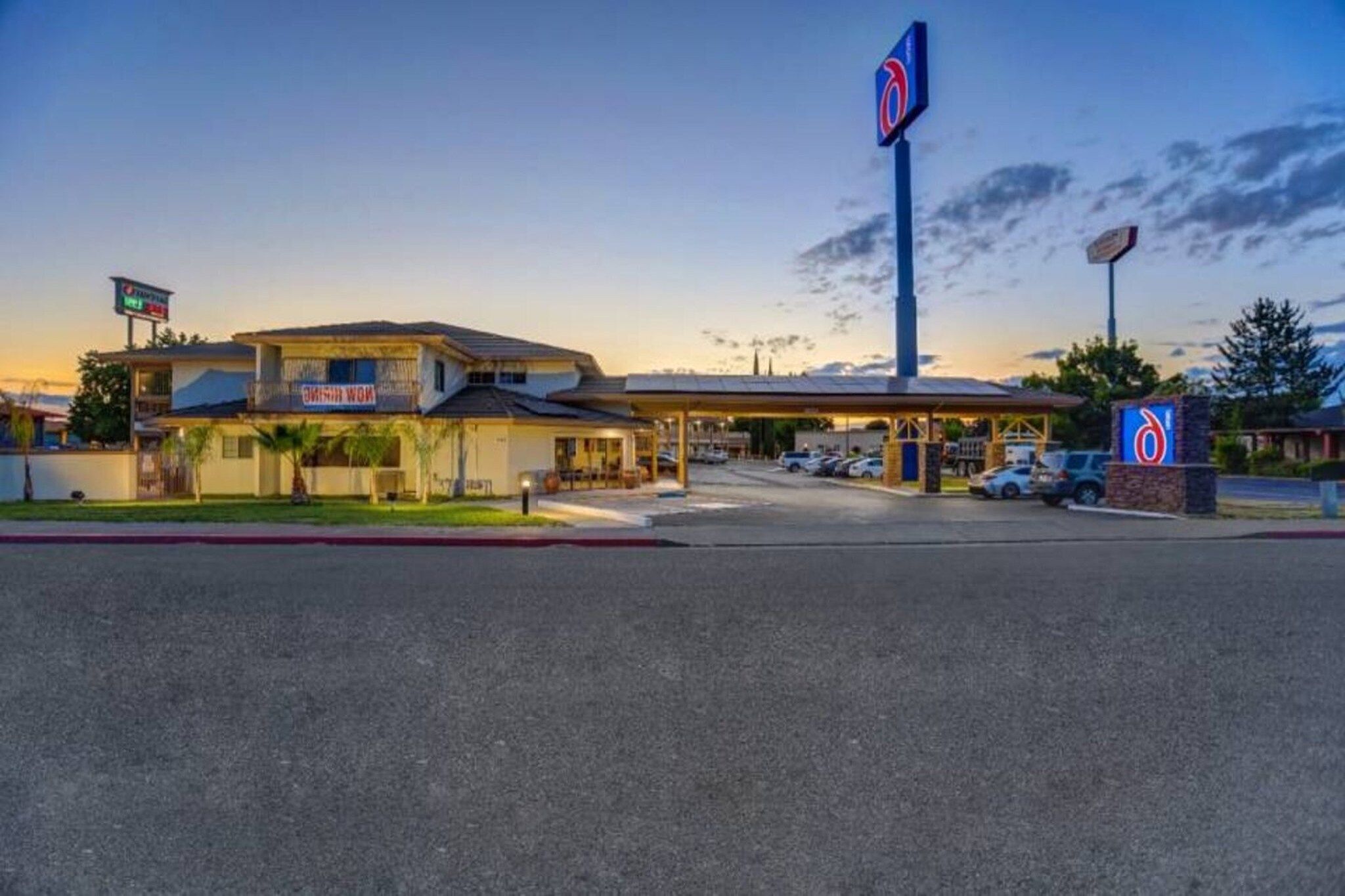 Um motel com posto de gasolina, uma placa grande e um estacionamento.