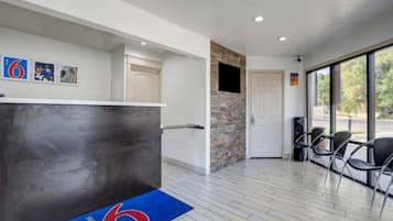 A reception area with a reception desk, a blue carpet with a logo, a stone wall, and a door leading to a balcony with chairs.