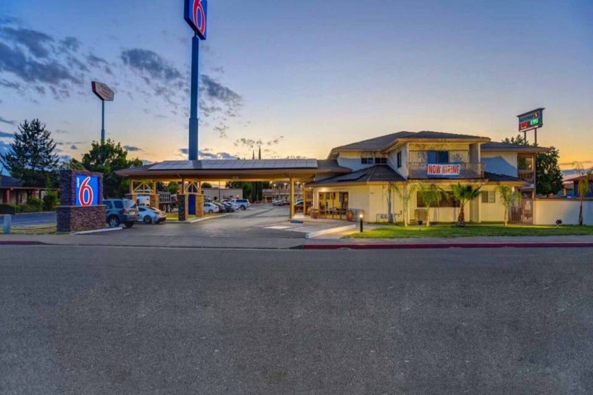 A motel with a gas station, a 'Now Hiring' sign, and a '6' sign indicating the location.