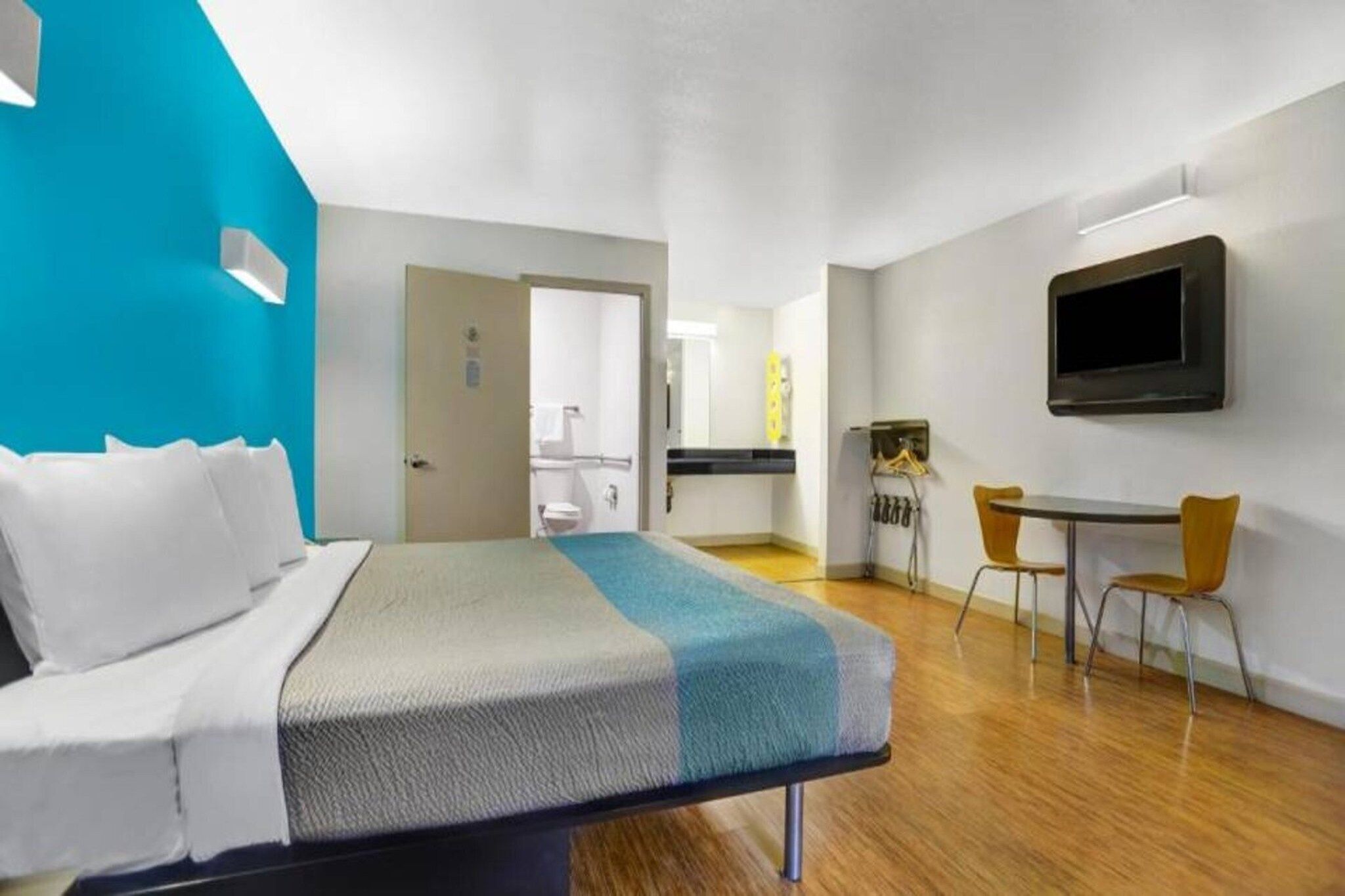 Ein Hotelzimmer mit Bett, Schreibtisch, Stuhl, Fernseher und einem durch eine geöffnete Tür einsehbaren Badezimmer.