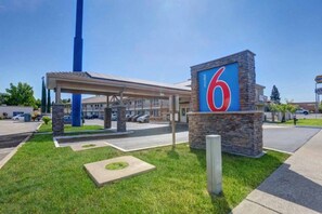 Um motel com um grande letreiro em formato de '6', área de estacionamento coberta e gramado bem cuidado.