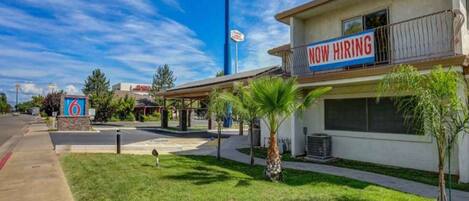 A motel with a 'Now Hiring' sign, a parking lot, and a clear blue sky.