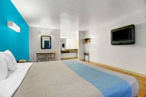 A hotel room with a bed, a desk, a chair, a television, and a bathroom.