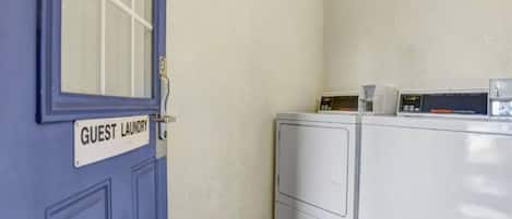 Un cuarto de lavandería con una puerta azul que indica 'LAVANDERÍA DE HUÉSPEDES' y una lavadora y secadora de carga frontal.