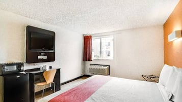 A hotel room with a bed, a desk, a television, a window with curtains, and a radiator.