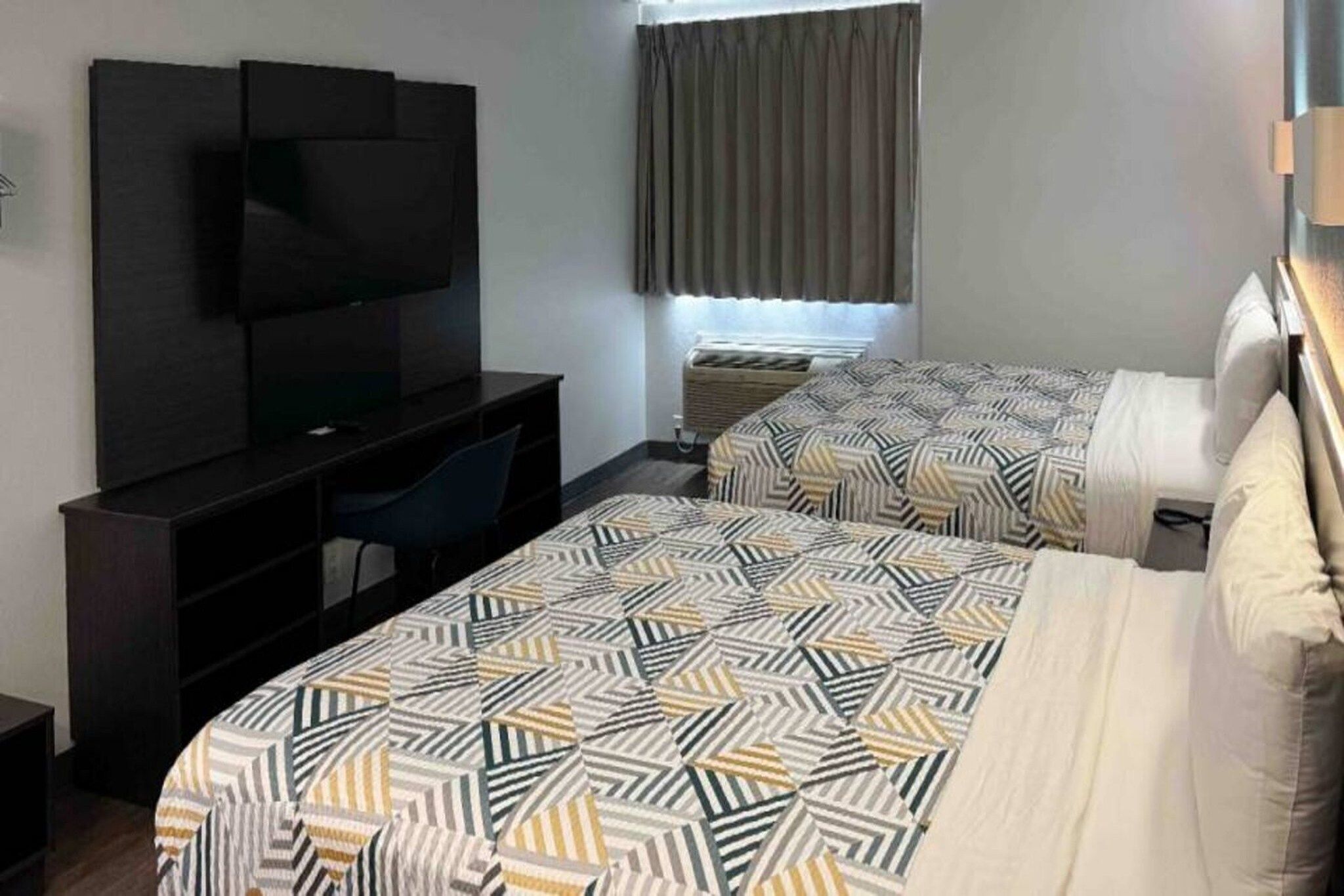 A hotel room with a bed, a desk, a chair, a television, and a window with curtains.