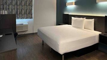 Una habitación de hotel con cama, mesitas de noche, un escritorio y cortina estampada.