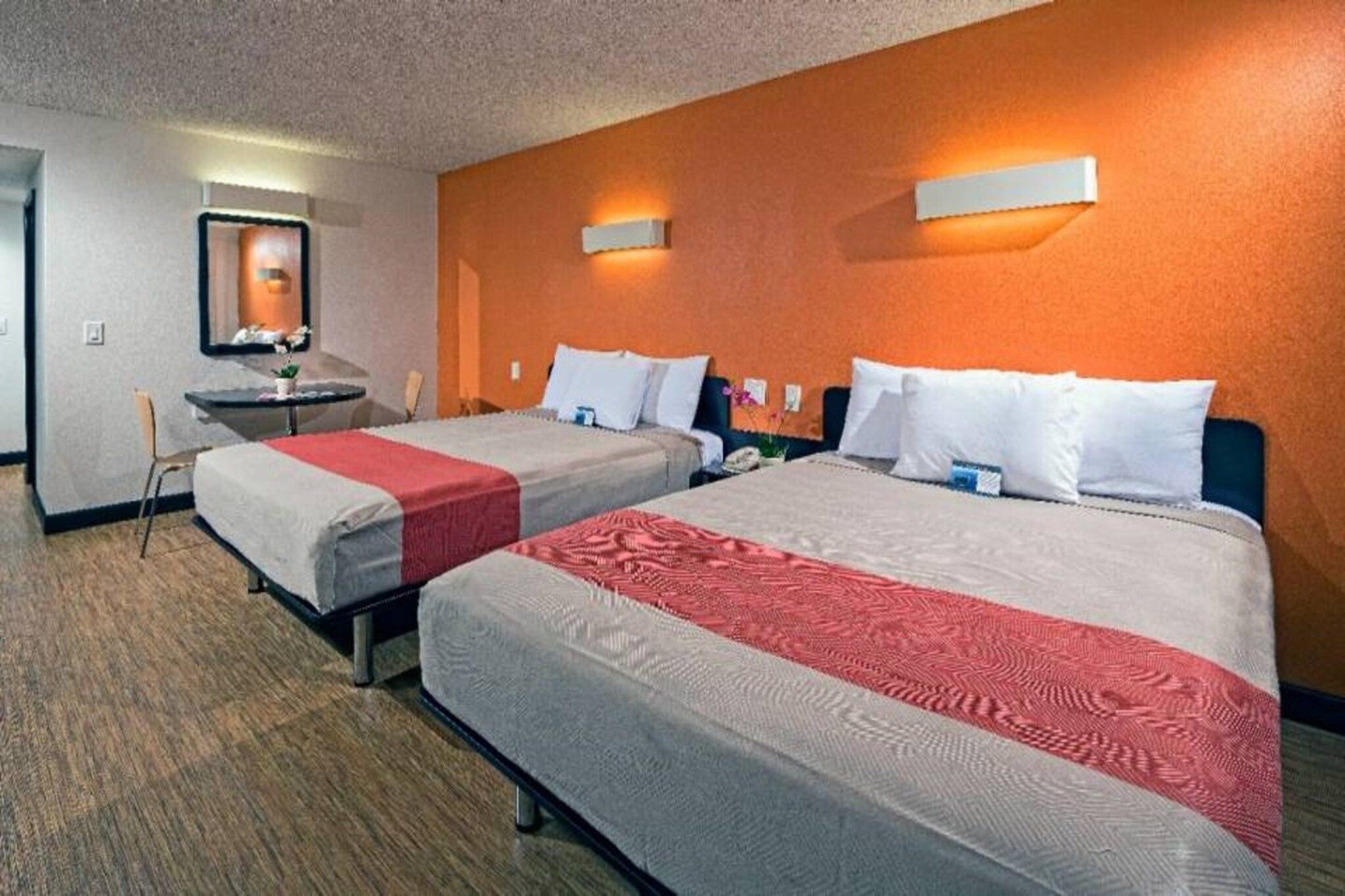 A hotel room with two beds, a small table, a chair, and a mirror.