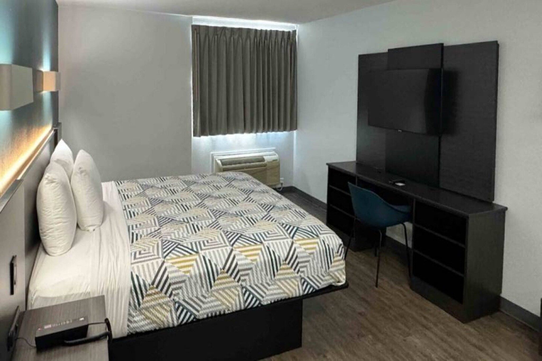 A hotel room with a bed, a desk, a chair, a TV, and a window with curtains.