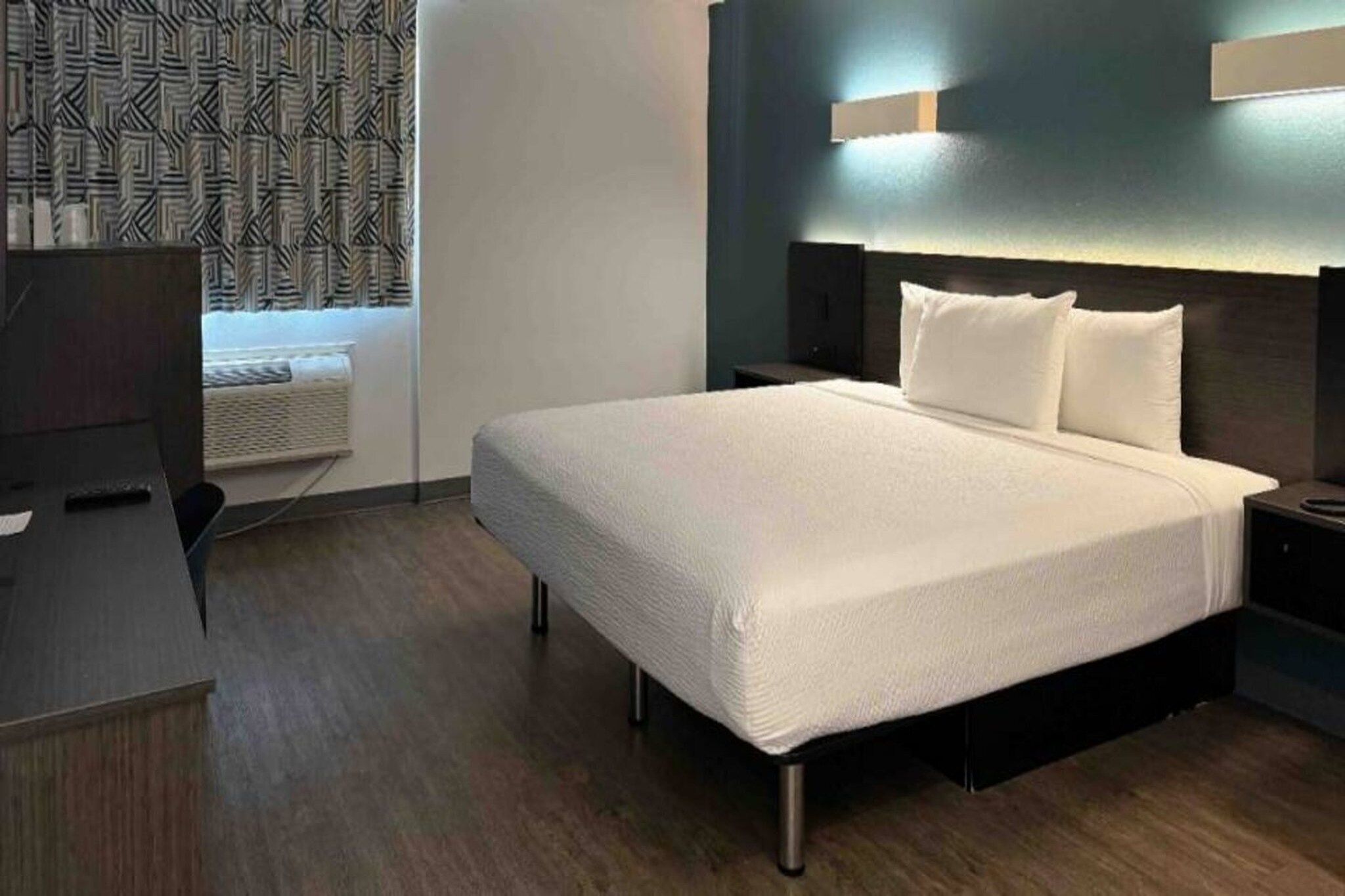 A hotel room with a bed, bedside tables, a desk, and a patterned curtain.