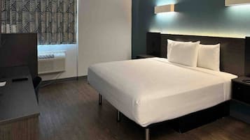A hotel room with a bed, bedside tables, a desk, and a patterned curtain.