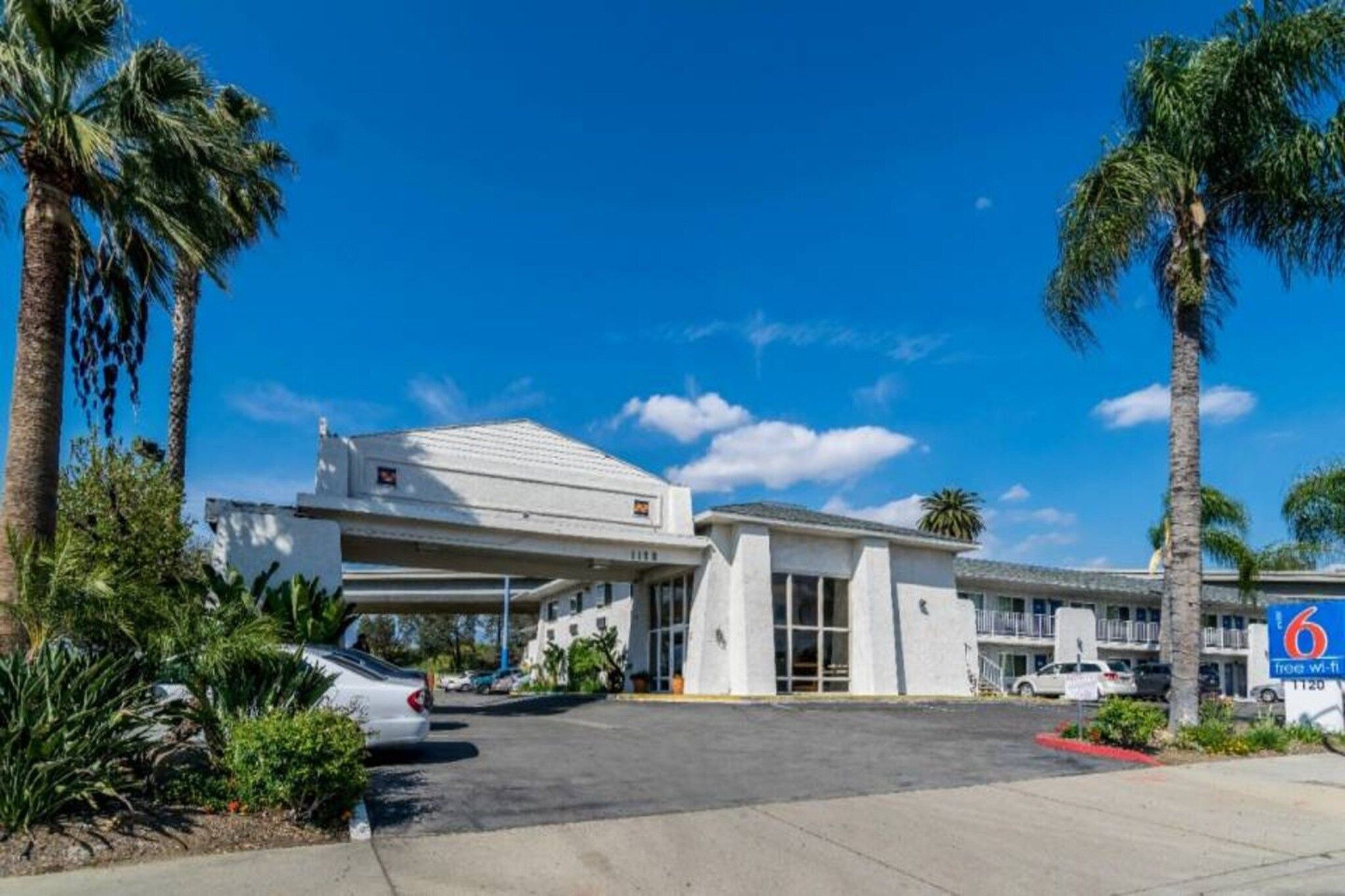 A motel with a covered parking area, palm trees, and a clear blue sky.