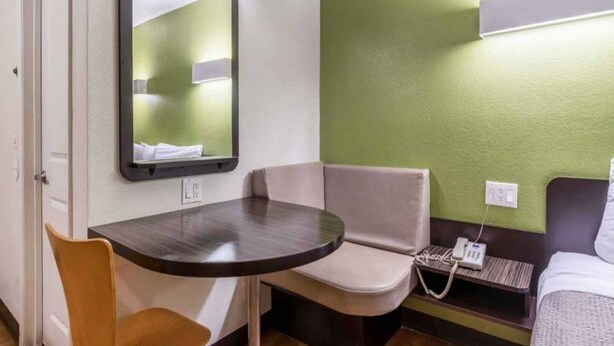 A compact hotel room with a single bed, a small table, a chair, a bedside table with a phone, and a mirror. - 1 QUEEN BED | NON-SMOKING (REDLANDS)