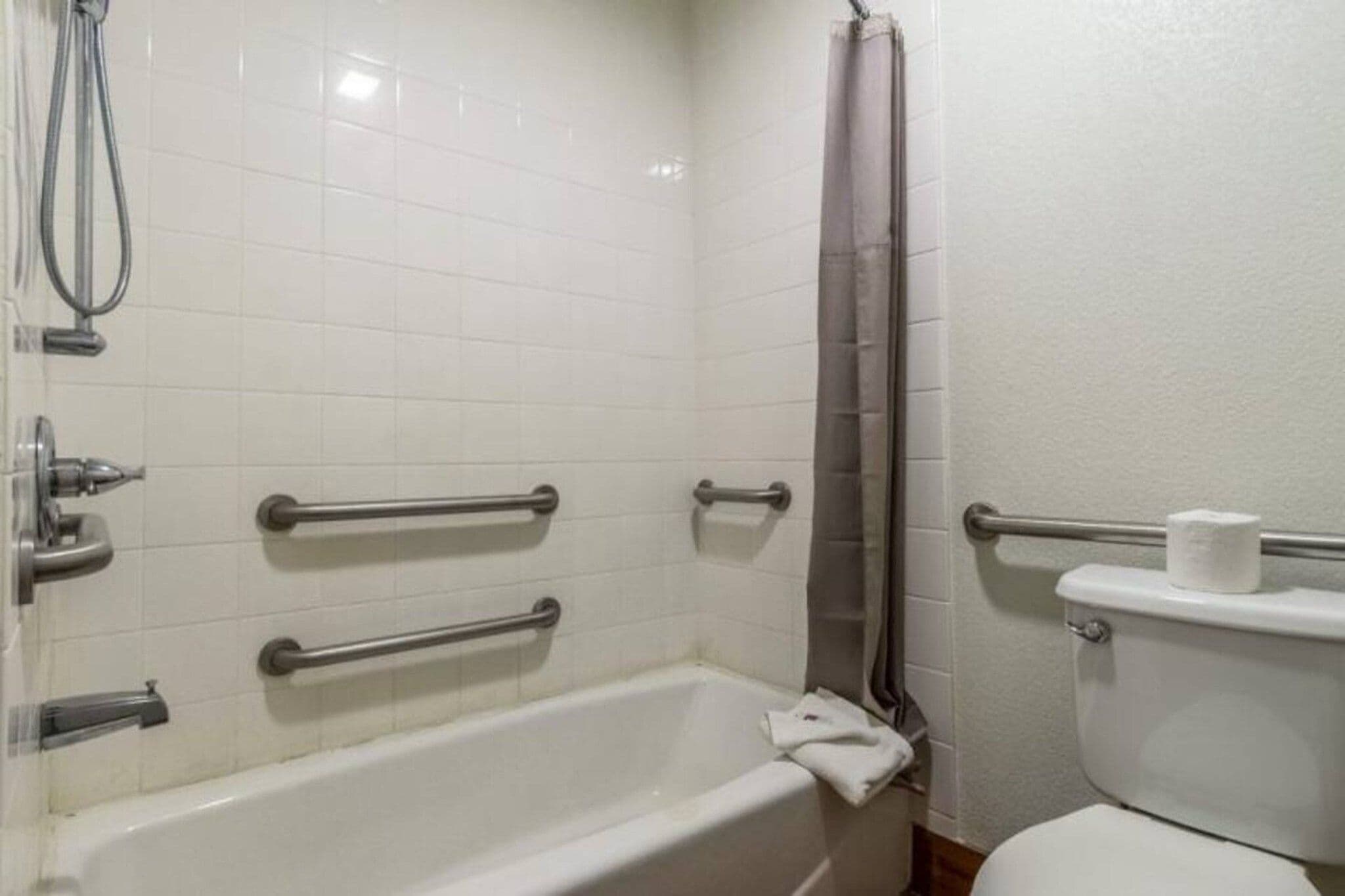 A bathroom with a bathtub, a shower, and a toilet. There are grab bars installed for safety.