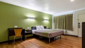 Habitación de hotel con cama, escritorio, silla, ventana con cortinas y puerta.