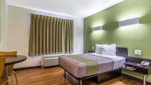 A hotel room with a bed, a desk, a chair, a window with curtains, and a wall-mounted air conditioner. - 1 QUEEN BED | NON-SMOKING (REDLANDS)